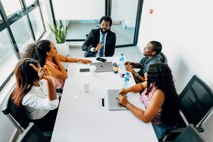 Business team meeting in modern office with leader presenting ideas around table with laptops and documents.