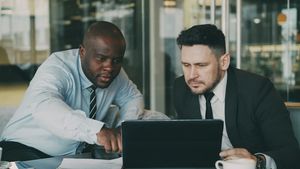 a black bald guy and a white guy wearing black tie looking at a laptop