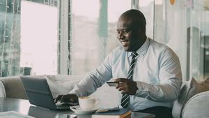a black bald business man wearing a tie smiling while using a laptop